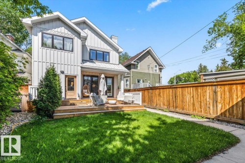 Rear exterior featuring a board and batten facade, multi-level wood deck, sliding patio doors, a privacy fence, and a manicured lawn - 10641 126 Street, Edmonton, AB 