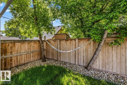 Landscaped backyard featuring mature trees, a wood privacy fence, and a stone border - 10641 126 Street, Edmonton, AB 