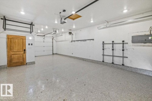 Spacious garage featuring a durable epoxy floor, recessed lighting, a light wood-finish door, and built-in wall-mounted shelving - 10641 126 Street, Edmonton, AB 