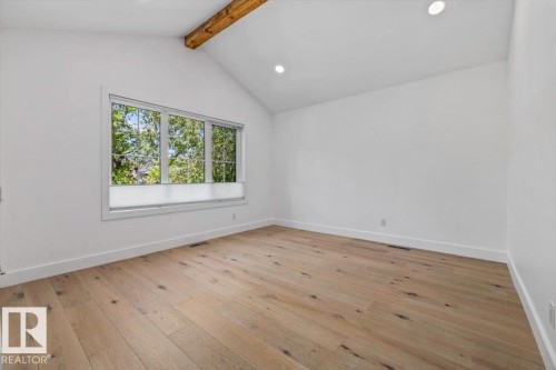 Spacious room featuring vaulted ceilings with exposed wood beams, recessed lighting, expansive window with tree-lined scenery, and wood-finish flooring - 10641 126 Street, Edmonton, AB 