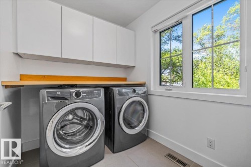 Laundry room featuring white shaker-style cabinetry, a wood-finish countertop, and a double-pane window - 10641 126 Street, Edmonton, AB 