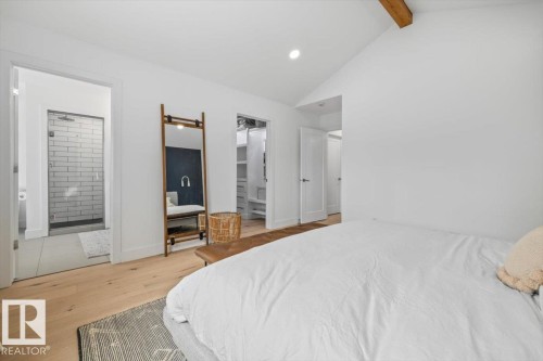 Bright interior space featuring wood-finish flooring, a vaulted ceiling with an exposed wood beam, a walk-in closet with built-in shelving, and a bathroom with a glass-enclosed subway tile shower - 10641 126 Street, Edmonton, AB 