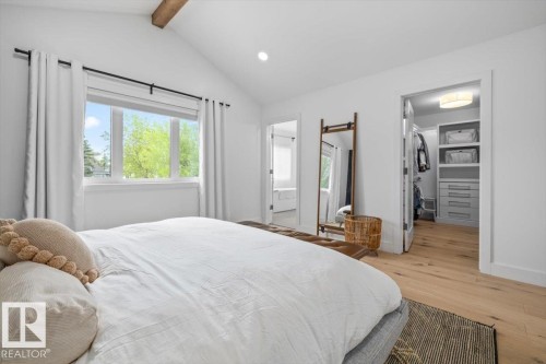 Bright bedroom featuring a vaulted ceiling with exposed wood beam, large window, and wood-finish flooring - 10641 126 Street, Edmonton, AB 
