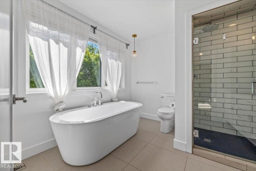 Freestanding soaking tub with chrome fixtures, set beneath large windows - 10641 126 Street, Edmonton, AB 