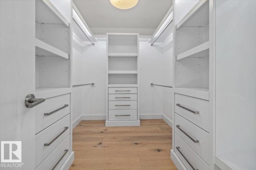Walk-in closet featuring custom white cabinetry, integrated shelving, multiple hanging rods, built-in drawer storage, and wood-finish flooring - 10641 126 Street, Edmonton, AB 