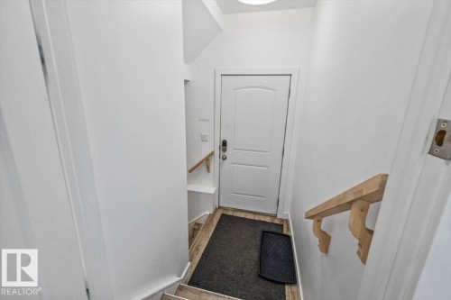 Lower level access featuring a white paneled door, wood-finish flooring, and a natural wood handrail with decorative corbels - 10641 126 Street, Edmonton, AB 