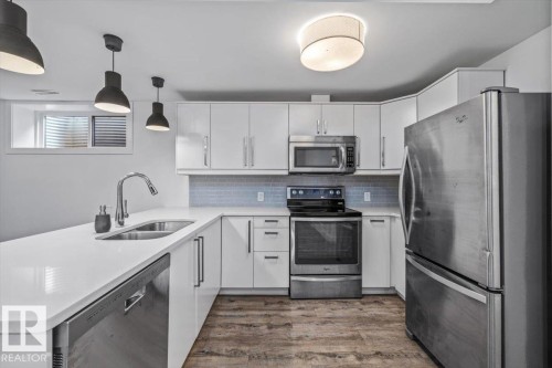 Modern kitchen featuring white cabinetry, stainless steel appliances, light-colored countertops, and wood-finish flooring - 10641 126 Street, Edmonton, AB 