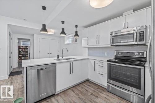 Modern kitchen featuring white cabinetry, stainless steel appliances, a white countertop, and wood-finish flooring - 10641 126 Street, Edmonton, AB 