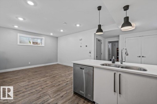 Kitchen island with white cabinetry, a double basin stainless steel sink, and a stainless steel dishwasher - 10641 126 Street, Edmonton, AB 