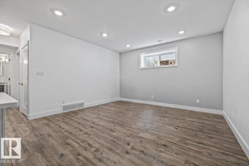Spacious room featuring wood-finish flooring, recessed lighting, a white trim window, and white baseboards - 10641 126 Street, Edmonton, AB 