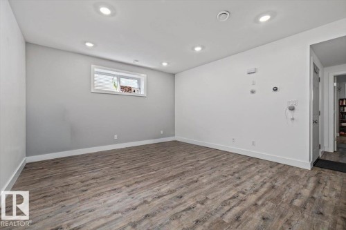 Spacious room featuring wood-finish flooring, recessed ceiling lighting, a window with white blinds, and crisp white baseboards - 10641 126 Street, Edmonton, AB 