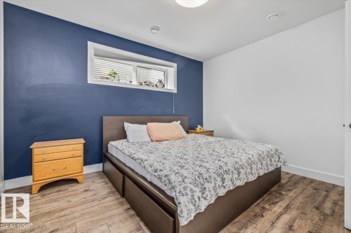Interior room featuring wood-finish flooring, a white trim baseboard, a recessed window, and white walls complemented by a single accent wall - 10641 126 Street, Edmonton, AB 