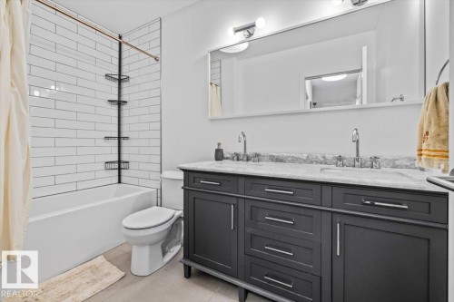 Bathroom featuring a white subway tile surround shower-tub combination with a bronzed shower rod, a dual-sink vanity with a grey cabinet base, a light-toned countertop, and chrome fixtures - 10641 126 Street, Edmonton, AB 
