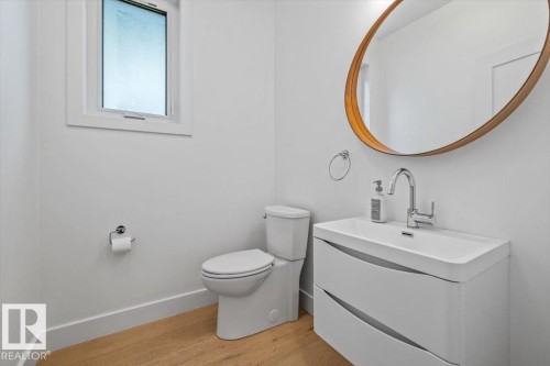 Modern powder room featuring a white floating vanity with an integrated sink, a chrome faucet, and a large oval mirror with a wood-finish frame - 10641 126 Street, Edmonton, AB 