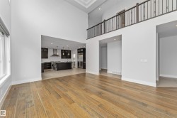 Expansive living area featuring wood-finish flooring, a soaring two-story ceiling, and a second-story balcony with metal railings - 