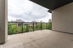 Outdoor balcony featuring a textured concrete floor, clear glass railings with black metal framing, and a stucco exterior wall - 