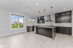Modern kitchen featuring a large waterfall-edge island, dark cabinetry with glass accents, stainless steel range hood, recessed lighting, and tile flooring - 