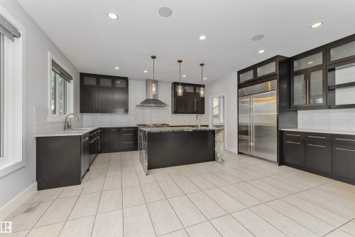 Open-concept kitchen featuring dark wood cabinetry, stainless steel appliances, a center island with a waterfall countertop, recessed lighting, and large format tile flooring - 3310 Watson Bay, Edmonton, AB 