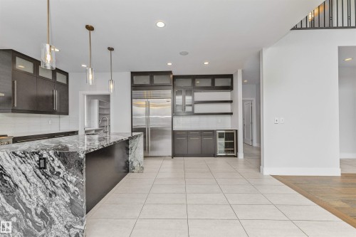 Gourmet kitchen featuring a large island with a waterfall edge, dark wood-finish cabinetry, stainless steel appliances, a beverage cooler, and pendant lighting - 3310 Watson Bay, Edmonton, AB 
