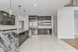 Gourmet kitchen featuring a large island with a waterfall edge, dark wood-finish cabinetry, stainless steel appliances, a beverage cooler, and pendant lighting - 