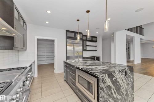 Kitchen featuring a large waterfall island with integrated microwave, stainless steel appliances, contemporary pendant lighting, and a walk-in pantry with extensive shelving - 3310 Watson Bay, Edmonton, AB 