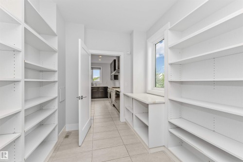 Spacious pantry featuring extensive built-in shelving, tile flooring, a window providing natural light, and a built-in countertop surface - 3310 Watson Bay, Edmonton, AB 