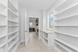 Spacious pantry featuring extensive built-in shelving, tile flooring, a window providing natural light, and a built-in countertop surface - 