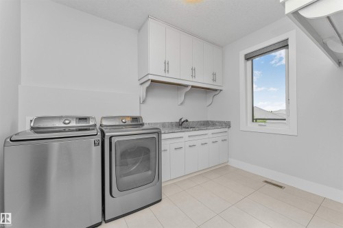 Functional laundry room featuring a utility sink, white cabinetry with silver hardware, and a light-toned tile floor - 3310 Watson Bay, Edmonton, AB 