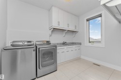 Functional laundry room featuring a utility sink, white cabinetry with silver hardware, and a light-toned tile floor - 