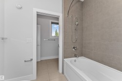 Contemporary bathroom featuring a white bathtub with chrome fixtures and light-toned tile surround - 
