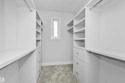 Walk-in closet with custom built-ins featuring white shelving, integrated drawers with brushed nickel hardware, multiple hanging rods, and a window providing natural illumination - 