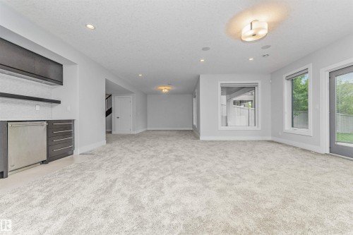 Spacious room featuring new carpeting, recessed lighting, and a built-in wet bar with dark wood-finish cabinetry and a stainless steel undercounter appliance - 3310 Watson Bay, Edmonton, AB 