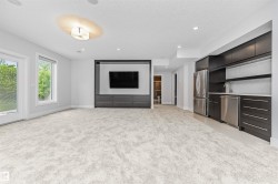 Spacious entertainment area featuring light-toned carpeting, a built-in media center with integrated cabinetry, and a wet bar complete with stainless steel appliances, dark wood-finish cabinetry, and a light-toned countertop - 