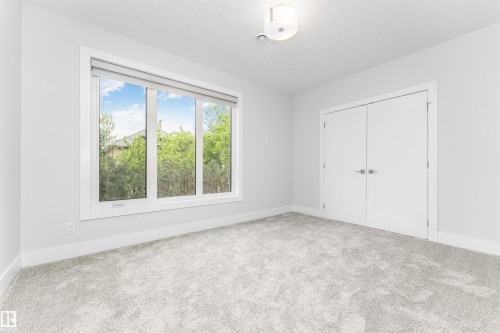 Bright interior space featuring a large three-panel window with roller shades, light grey carpet, white trim, and double white doors with modern hardware - 3310 Watson Bay, Edmonton, AB 