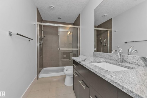 Bathroom featuring a spacious walk-in shower with glass enclosure, a vanity with a light-toned granite countertop, dual undermount sinks, and a large mirror - 3310 Watson Bay, Edmonton, AB 