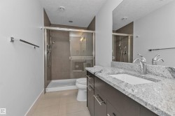 Bathroom featuring a spacious walk-in shower with glass enclosure, a vanity with a light-toned granite countertop, dual undermount sinks, and a large mirror - 