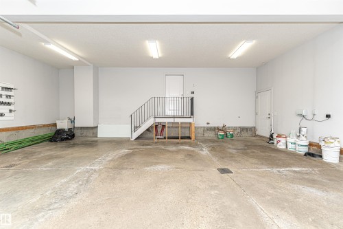 Spacious garage with concrete flooring, fluorescent overhead lighting, a utility sink, a built-in storage rack, and an interior staircase providing additional access - 3310 Watson Bay, Edmonton, AB 