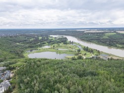 Expansive aerial panorama showcasing a meandering river, a golf course with multiple water features, and dense mature forest - 