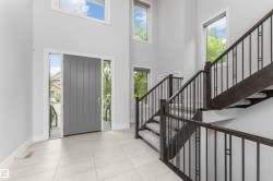 Two-story foyer featuring a gray panel door with sidelights, a custom dark wood-finish staircase with wrought iron railings, and light-toned tile flooring - 