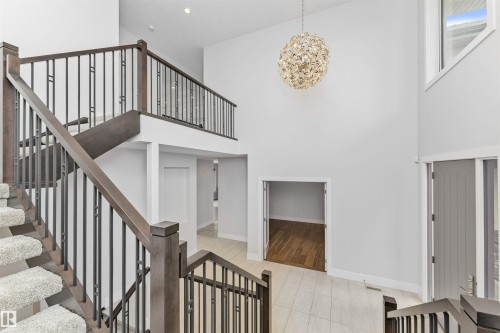 Two-story foyer featuring a contemporary chandelier, a multi-level staircase with wood-finish handrails and black metal balusters, and light-toned tile flooring - 3310 Watson Bay, Edmonton, AB 