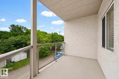 Private balcony featuring glass railings, a smooth finished floor, and textured stucco exterior - 203 10719 80 Avenue, Edmonton, AB 