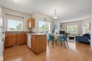Open-concept living area featuring wood-finish flooring, a kitchen with light wood cabinetry and a peninsula, a dining area with pendant lighting, a living room with a fireplace, and multiple windows with blinds - 203 10719 80 Avenue, Edmonton, AB 