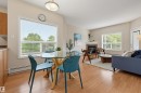 Open-concept living area featuring wood-finish flooring throughout, a glass-top dining table, and a built-in fireplace with a mantel - 203 10719 80 Avenue, Edmonton, AB 