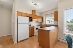 Kitchen featuring wood-finish flooring, wood cabinetry, white appliances, track lighting, and a window with blinds - 