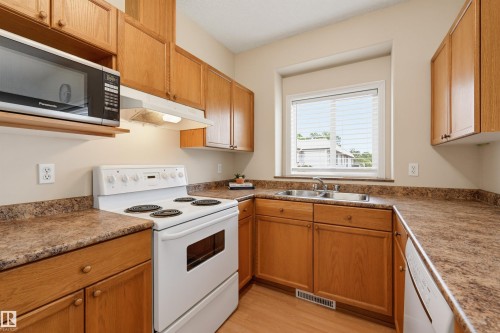Kitchen featuring wood cabinetry, laminate countertops, a double basin stainless steel sink, white electric range, and wood-finish flooring - 203 10719 80 Avenue, Edmonton, AB 