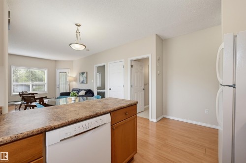 Kitchen featuring a white dishwasher integrated into wood cabinetry, a mottled countertop, and wood-finish flooring - 203 10719 80 Avenue, Edmonton, AB 