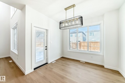 Bright interior space featuring wood-finish flooring, white trim, and a modern linear chandelier - 341 Roberts Wynd, Leduc, AB 