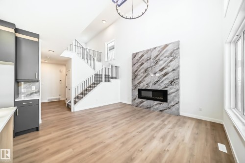 Expansive living space featuring high ceilings, wood-finish flooring, and a modern electric fireplace with a large format tile surround - 341 Roberts Wynd, Leduc, AB 