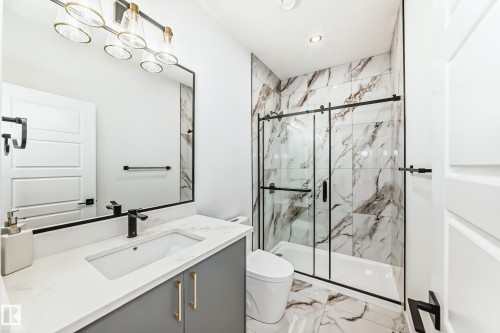 Modern bathroom featuring a single vanity with a white countertop and gray cabinetry, a black-framed mirror, and a contemporary light fixture - 341 Roberts Wynd, Leduc, AB 