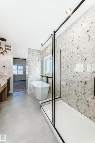 Contemporary bathroom featuring a freestanding tub, a walk-in shower with a glass enclosure, terrazzo-style tile walls, and large format floor tiles - 341 Roberts Wynd, Leduc, AB 